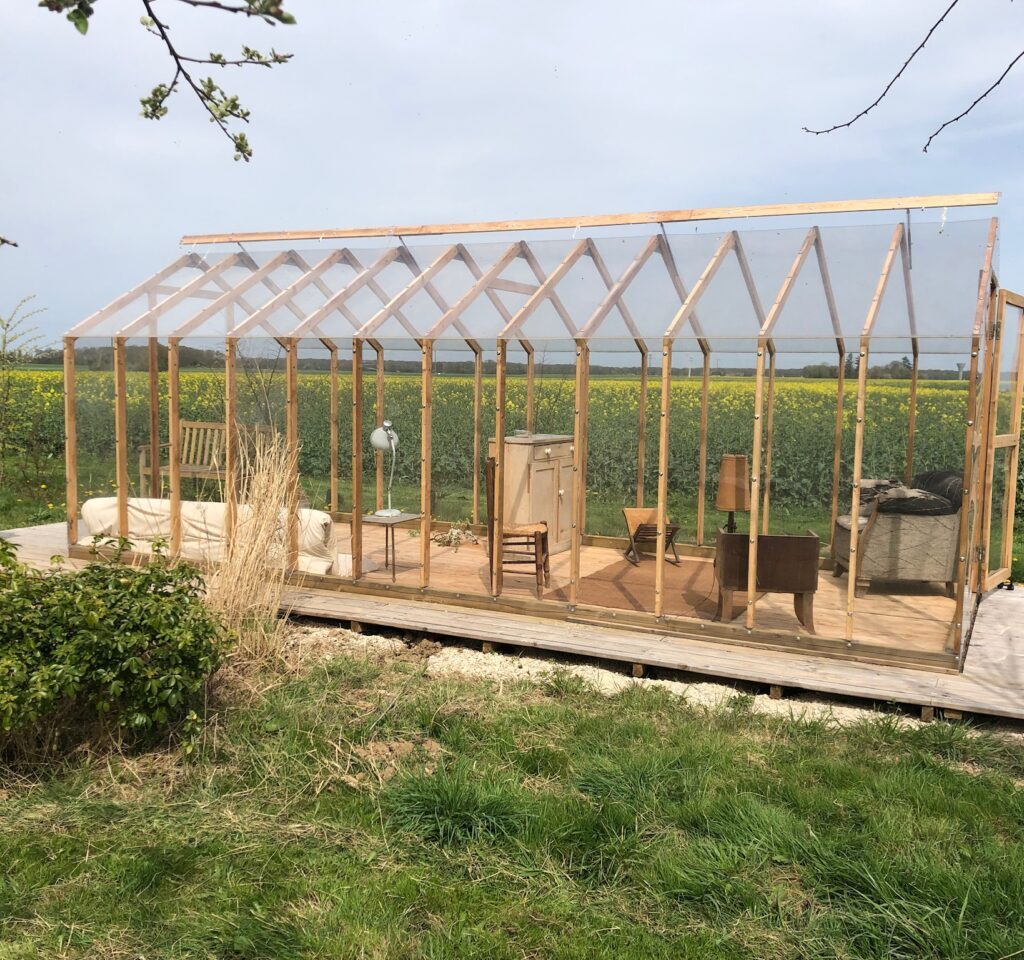 serre en bois transparente devant champ de colza